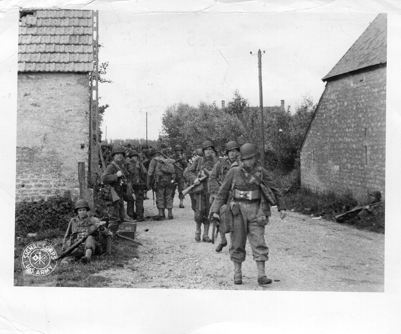 A file of Second World War infantry moving in spread formation through a damaged town