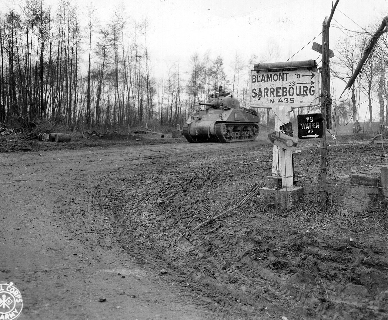 A Second World War medium tank moving along a village street past infantry