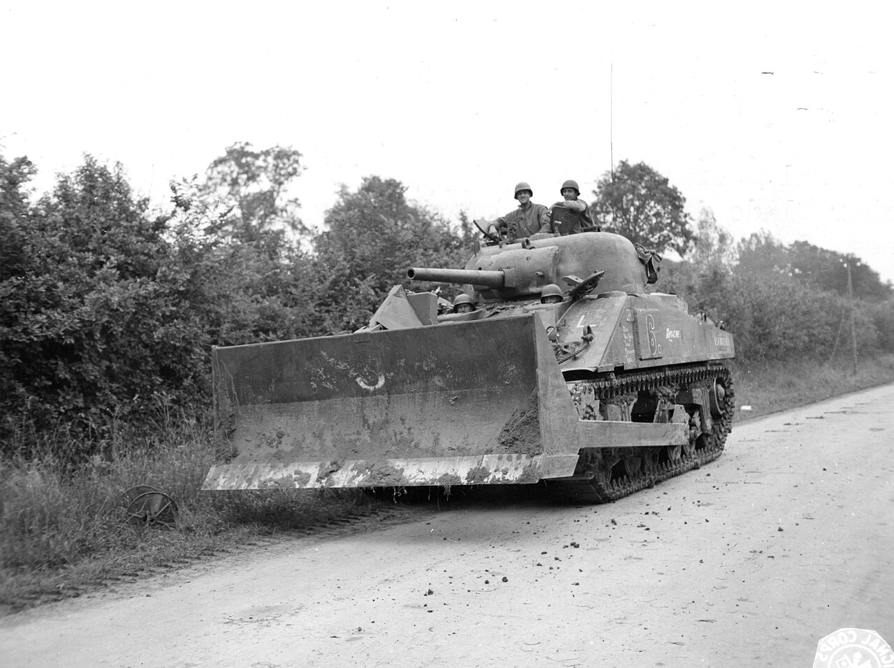 A Second World War medium tank fitted with a hedgerow cutting blade moving up a country lane